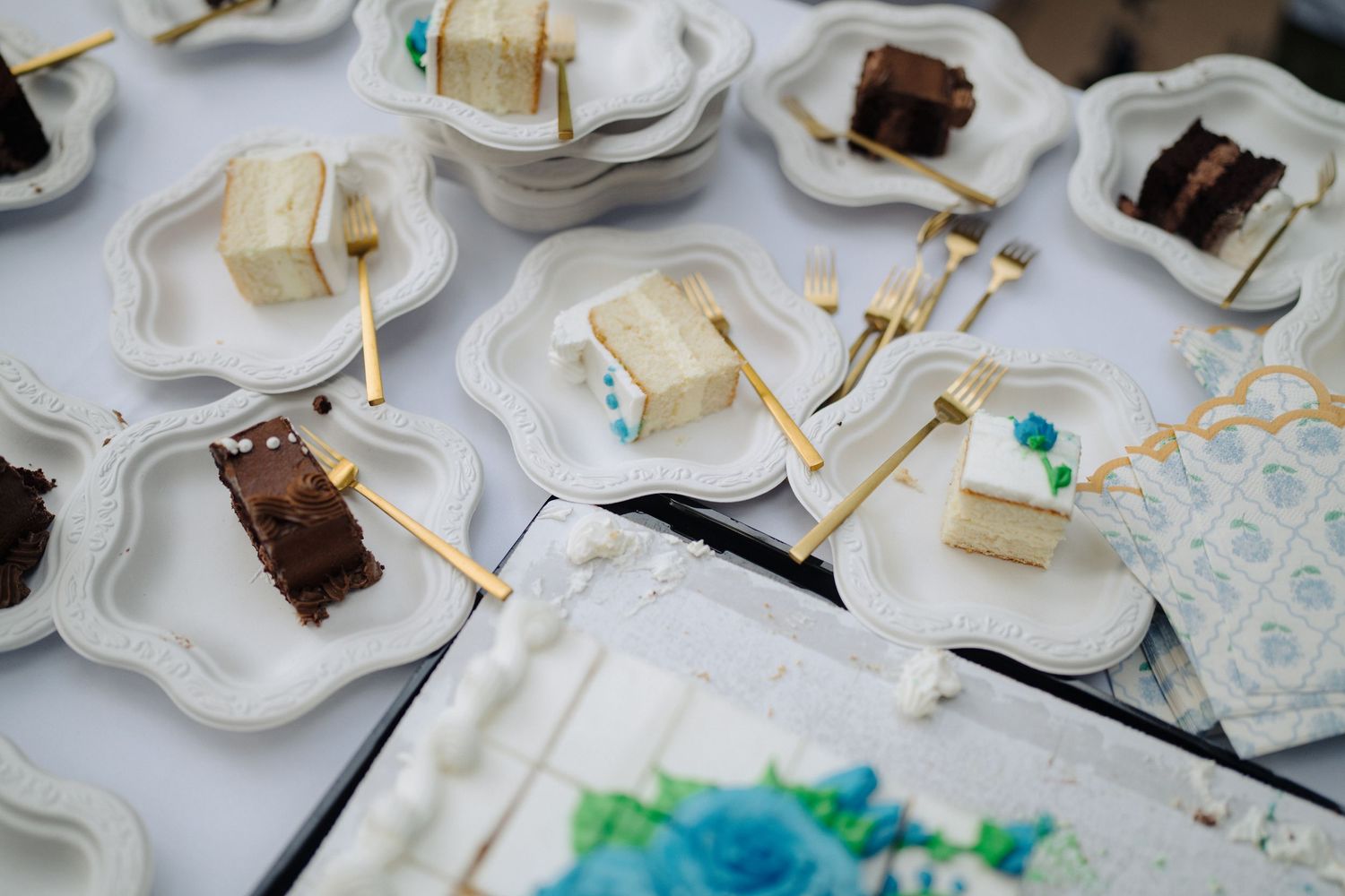 Wedding reception dessert table with chocolate and vanilla cake slices on decorative white plates.