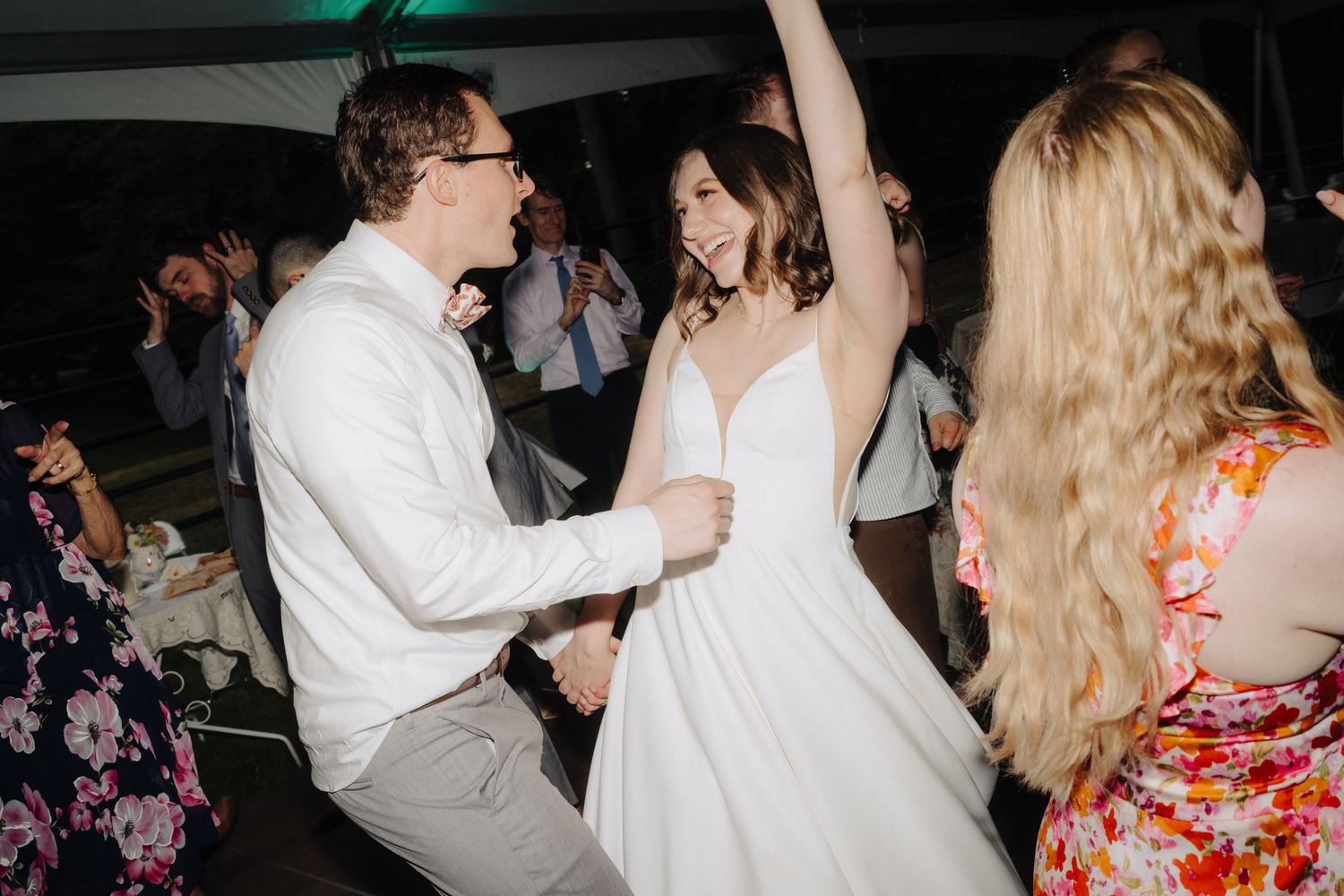 Energetic dancing at wedding reception with bride in white dress.