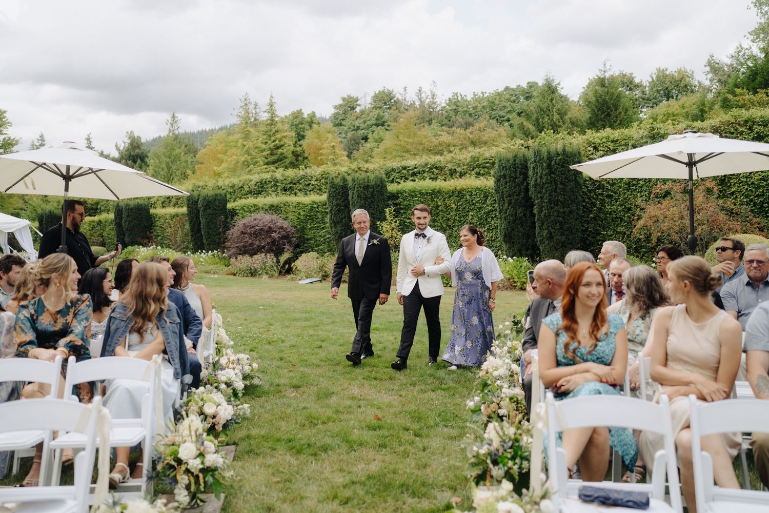 Outdoor wedding reception with white umbrellas and guests mingling on a grassy lawn.