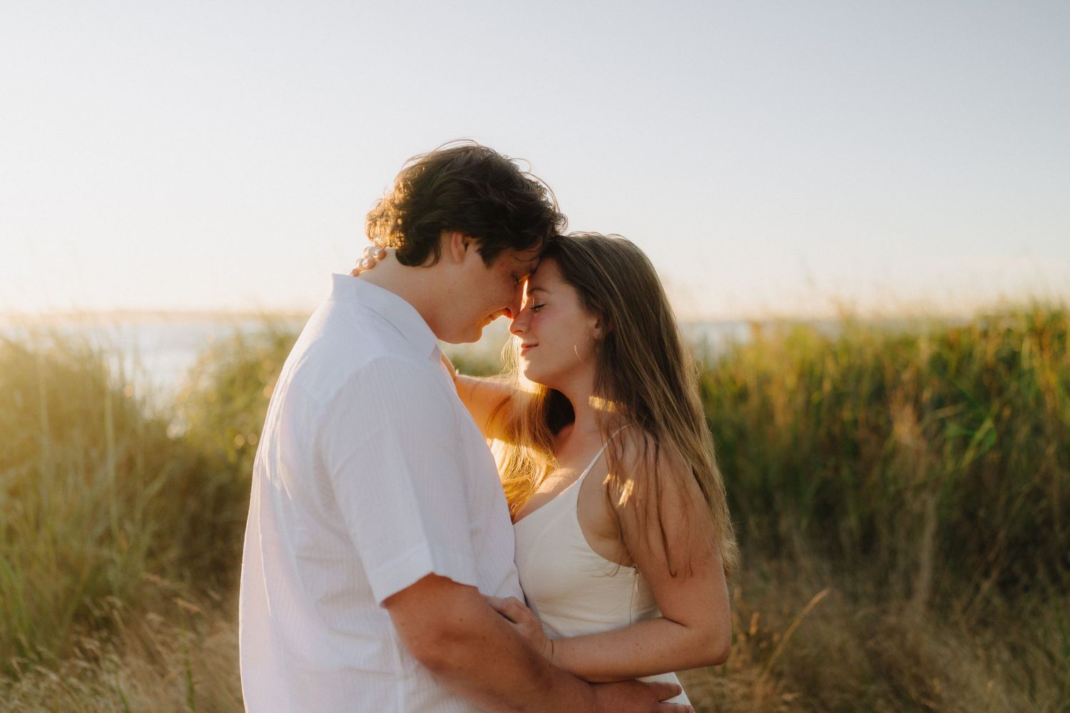 Couple embracing in a golden field during sunset with warm lighting.