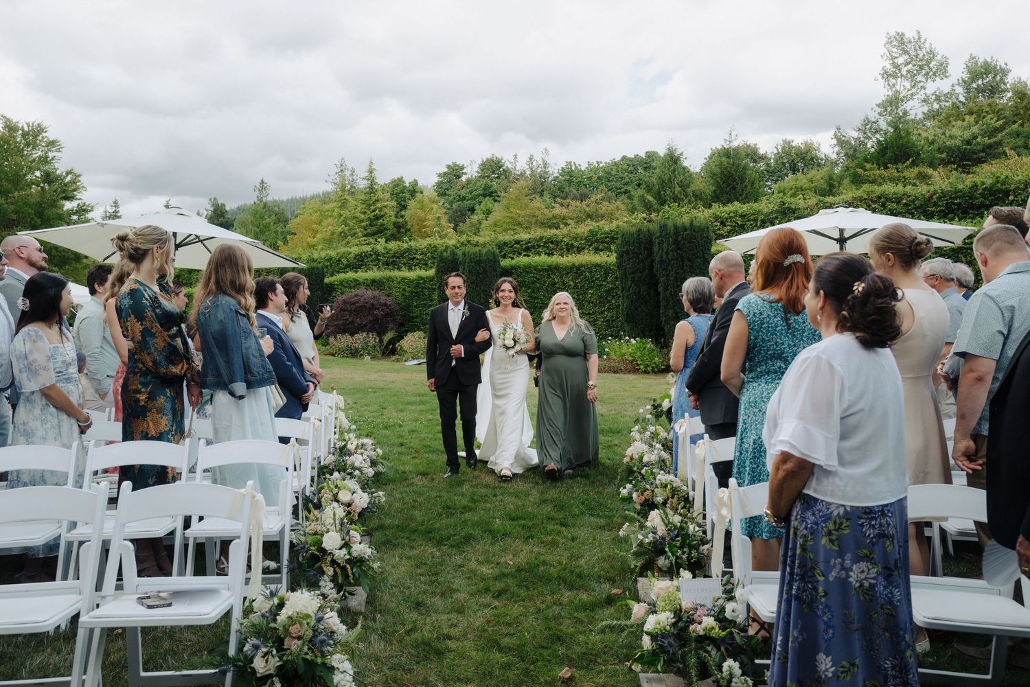 Garden wedding ceremony setup with white chairs and guests gathering under cloudy skies.