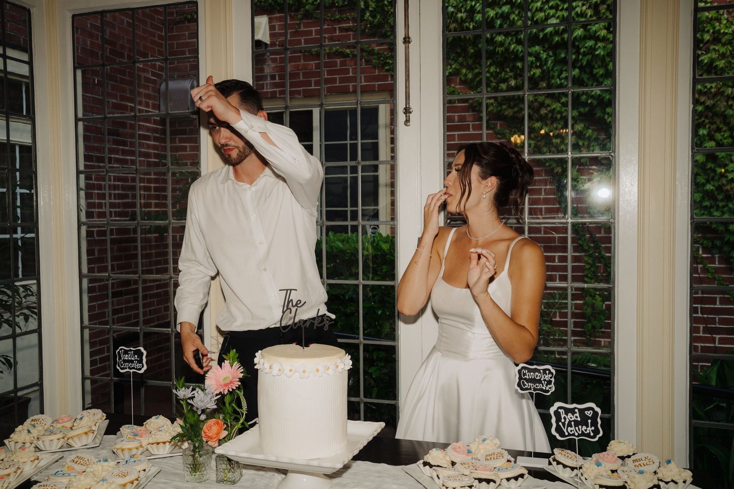 Couple playfully cutting their white wedding cake at indoor reception.
