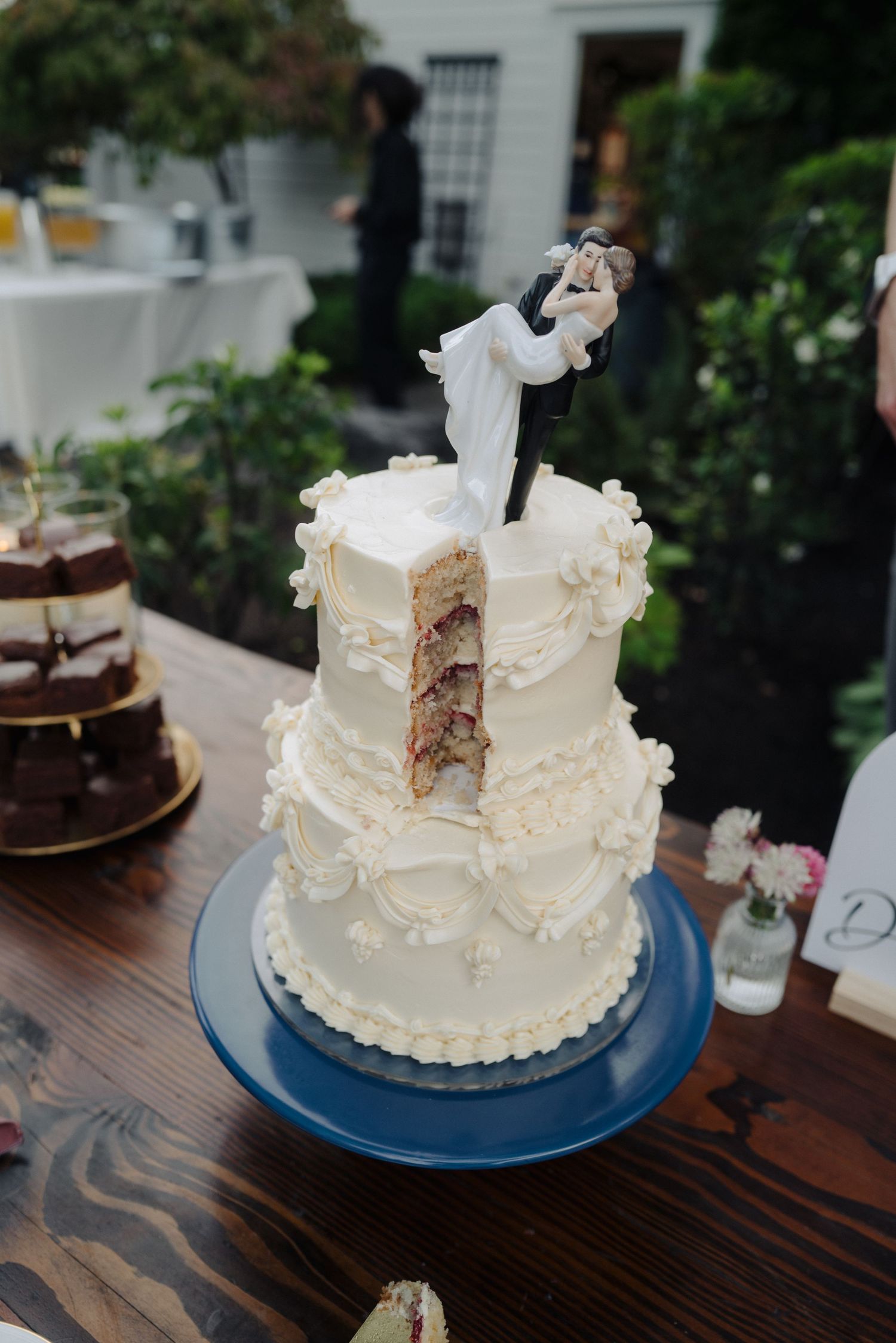 White wedding cake with delicate frosting details displayed on a blue plate at rustic wooden table.