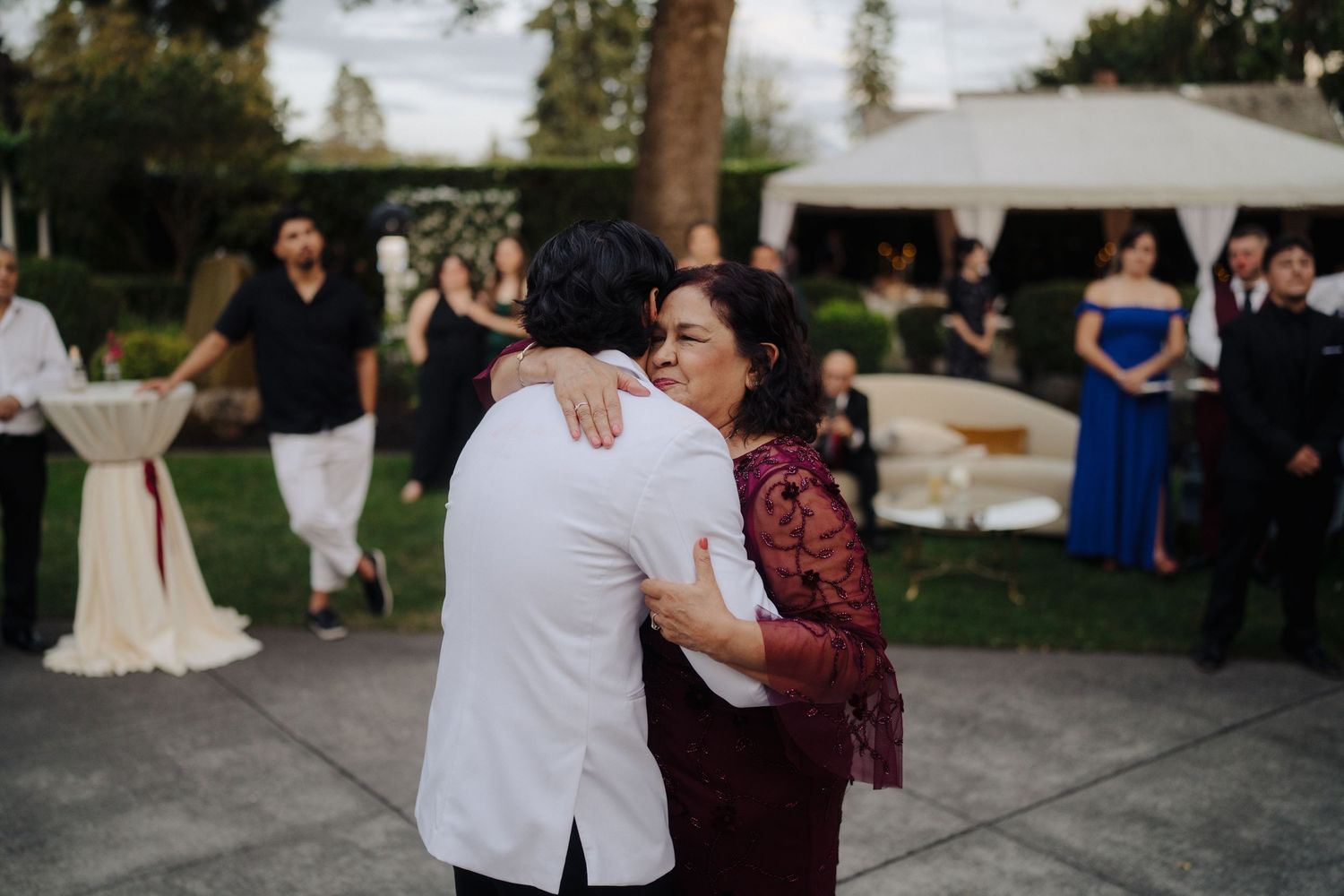 Guests dancing together during outdoor evening wedding celebration with white tent.