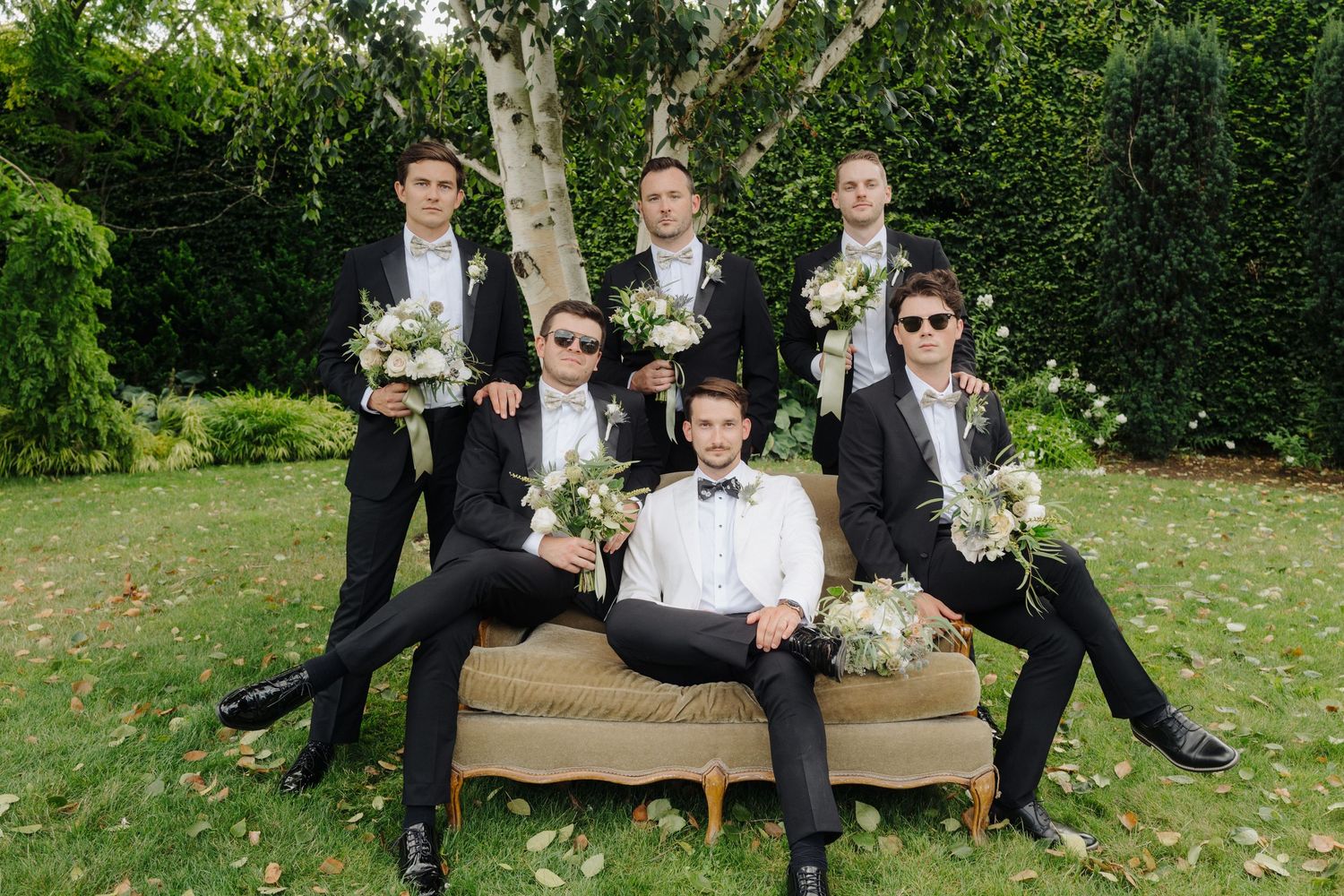Wedding party members relaxing on wooden benches in a sunny garden setting.