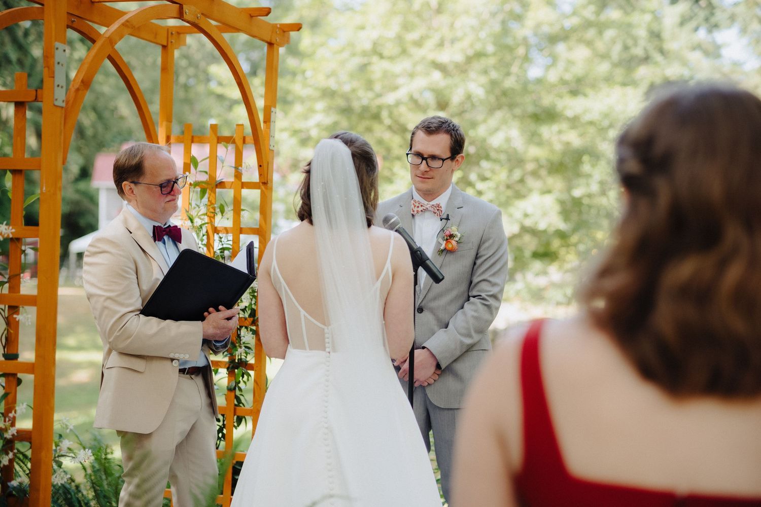 Outdoor wedding ceremony under wooden arch with guests seated in forest setting.