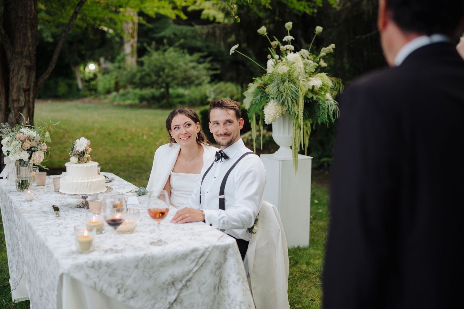Reception dinner scene with couple seated at decorated table in garden setting.