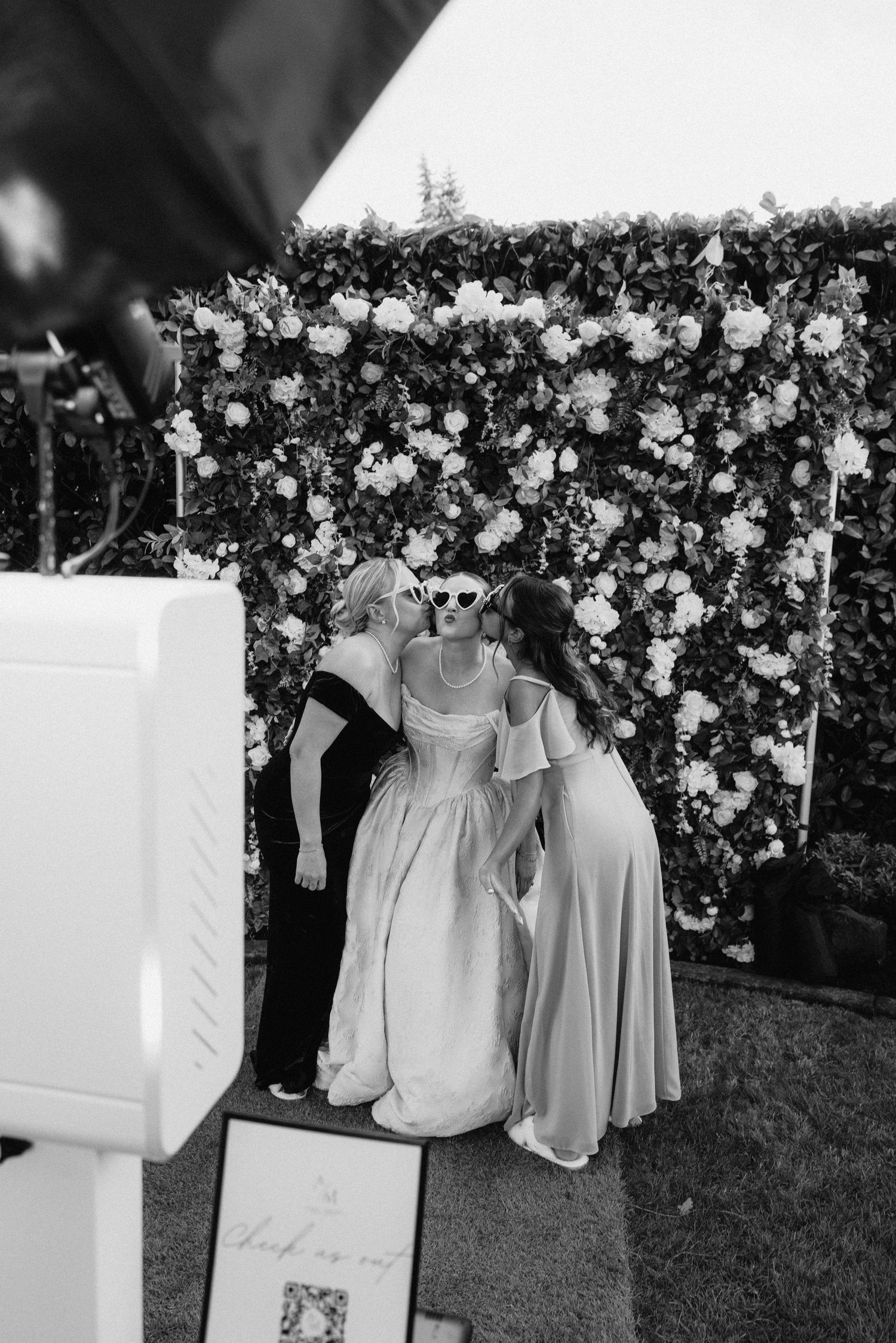 Black and white photo of wedding party against a floral wall backdrop.