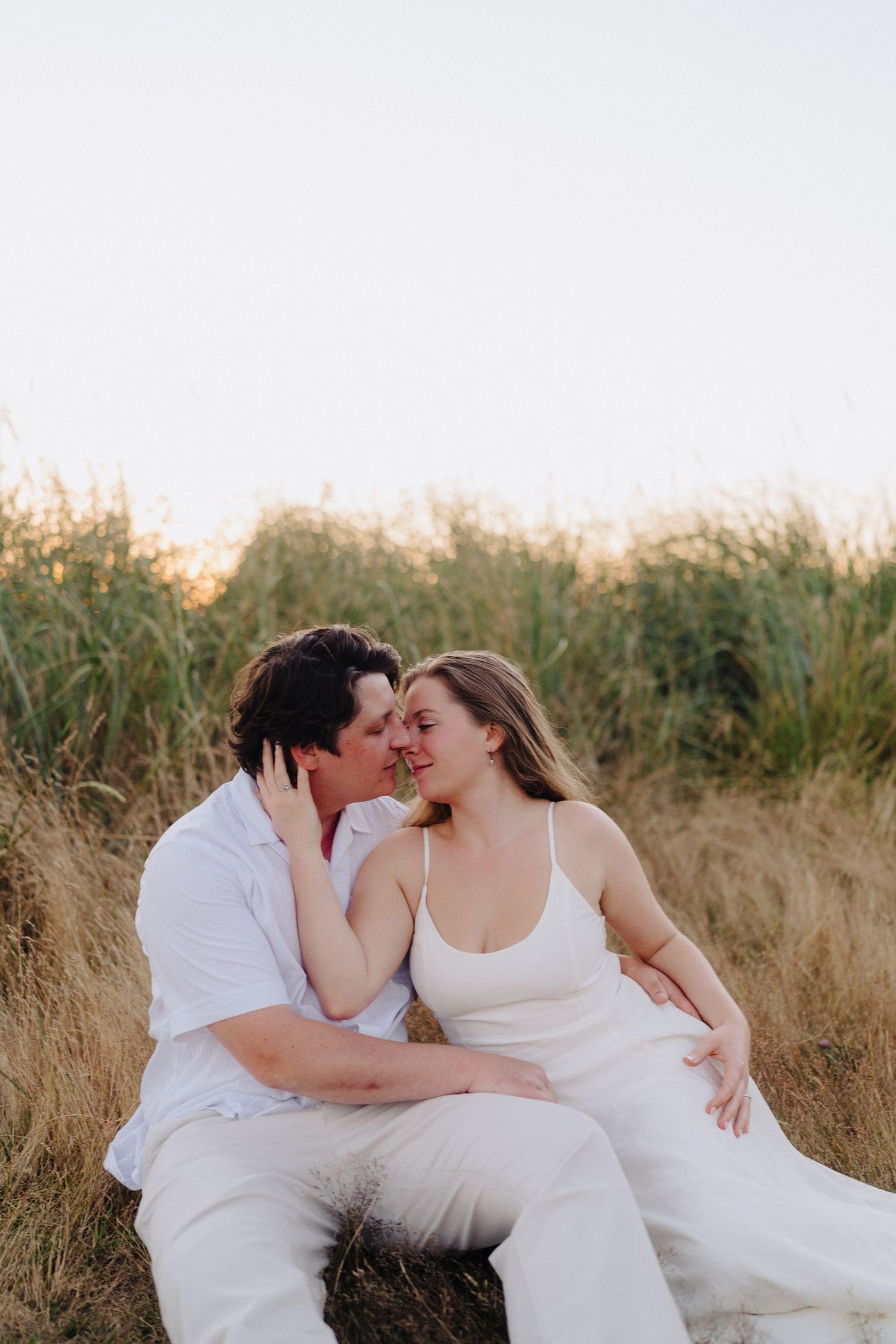 An intimate moment between a couple lying in tall grass wearing matching white outfits.