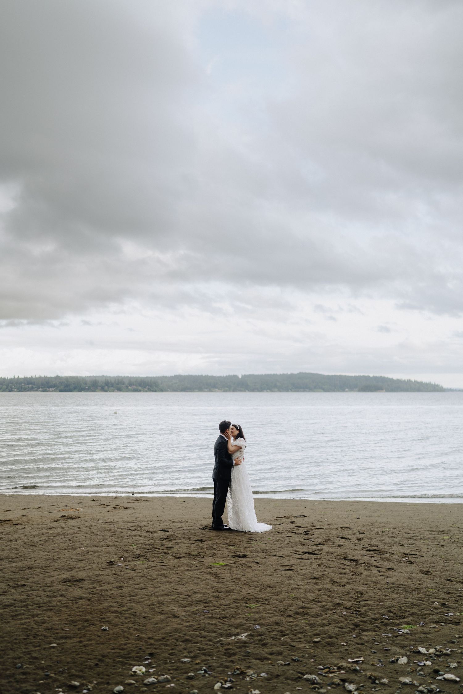 Couple shares intimate moment on a moody beach with cloudy skies and ocean backdrop.