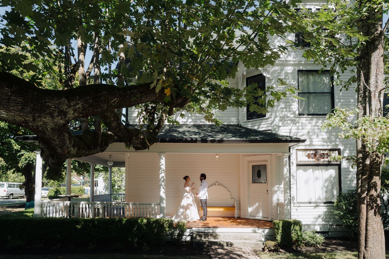 Exterior view of a white house with trees and greenery surrounding it in bright daylight.