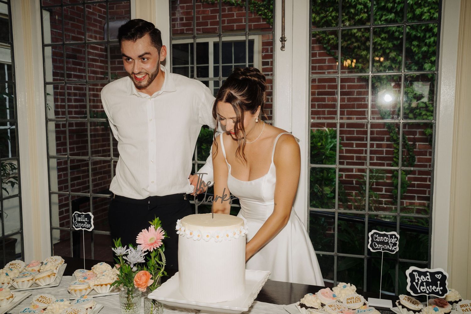 Wedding reception details with cake cutting and champagne toasts in front of brick windows.