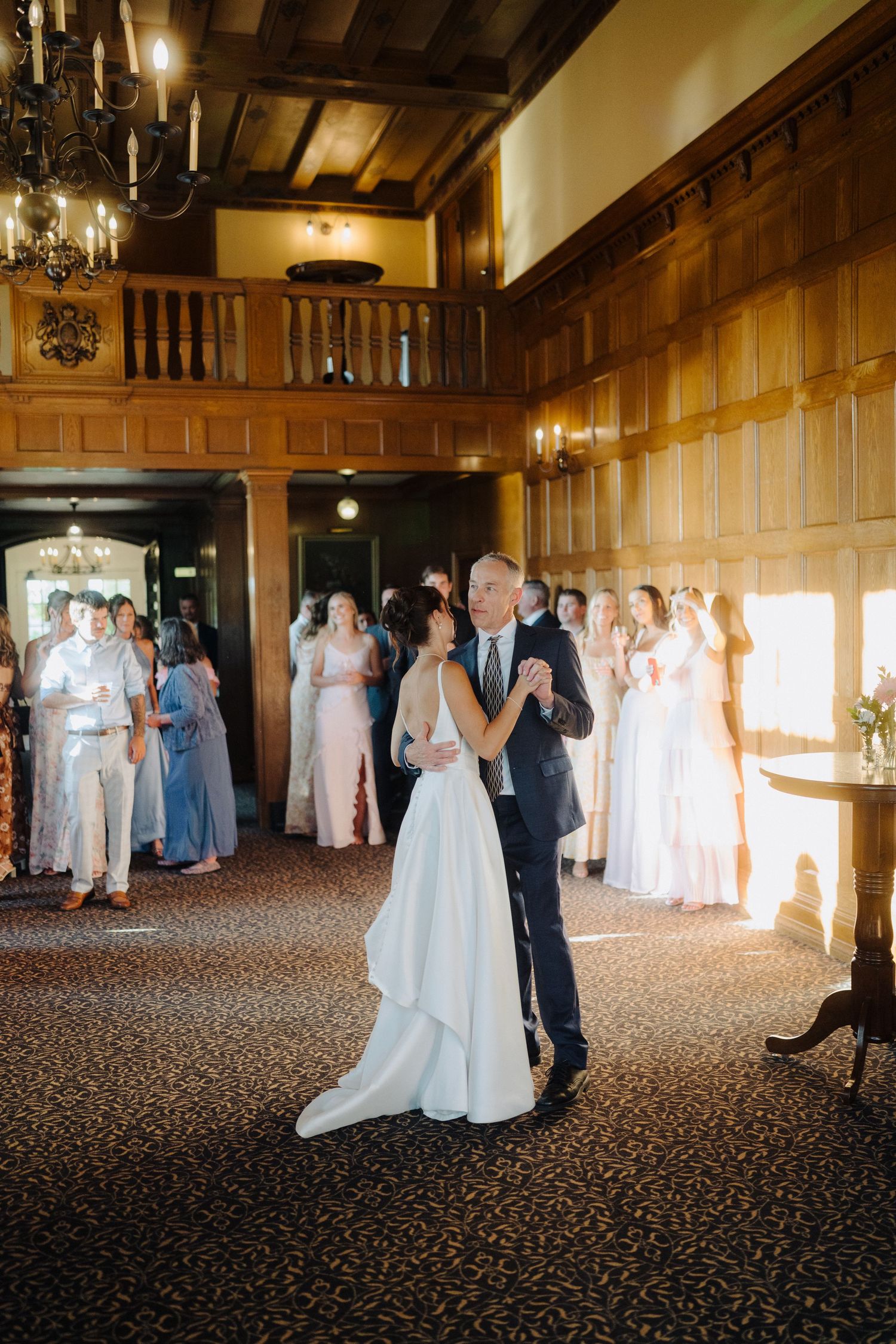 Wedding reception in an elegant wood-paneled ballroom with guests dancing and mingling.