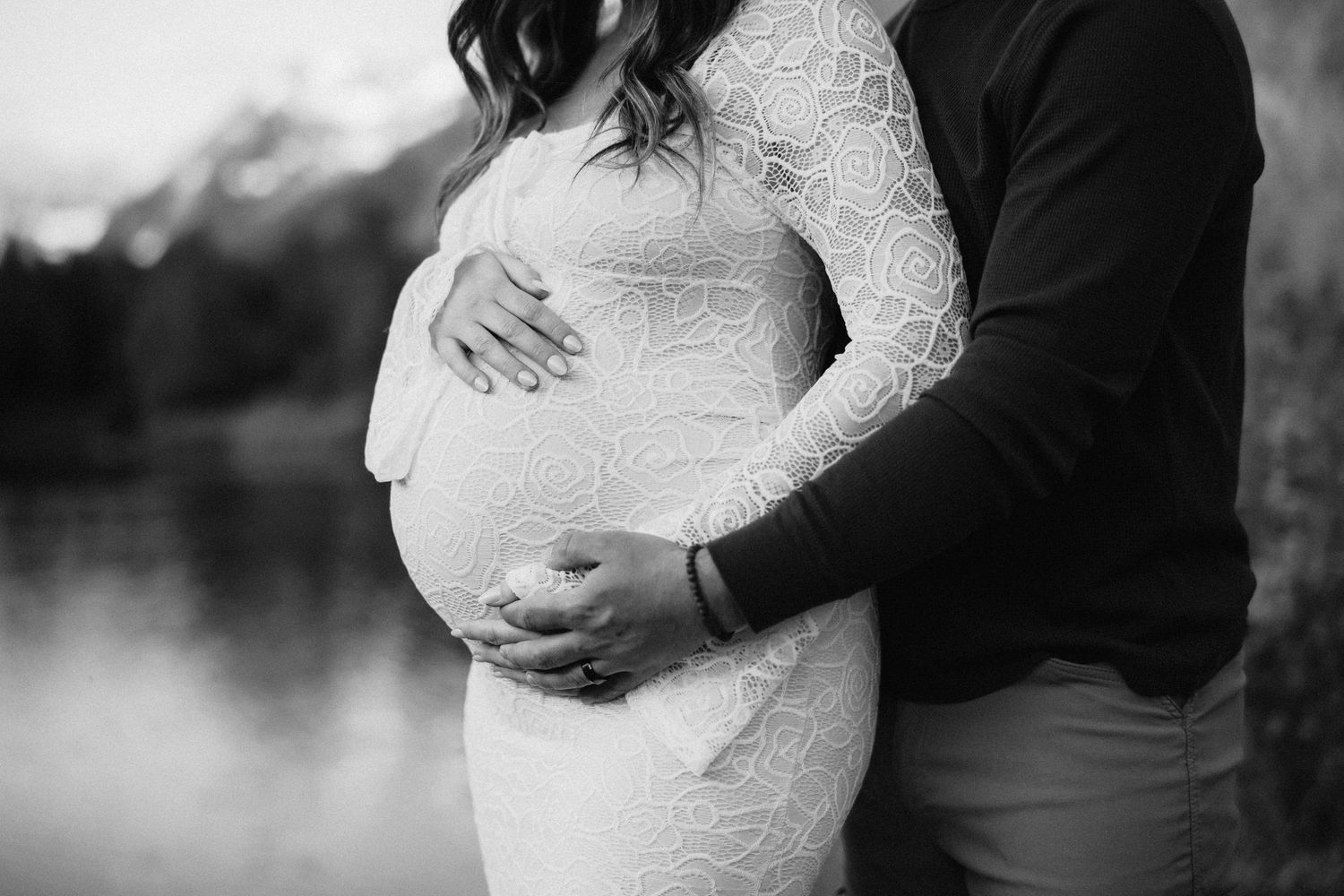 A black and white maternity photo showing gentle embrace by a misty lake.