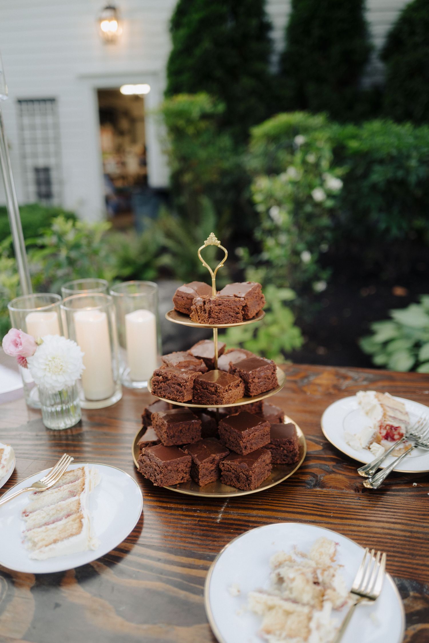 Reception dessert table with chocolate brownies and cake slices on wooden surface with glowing lanterns.
