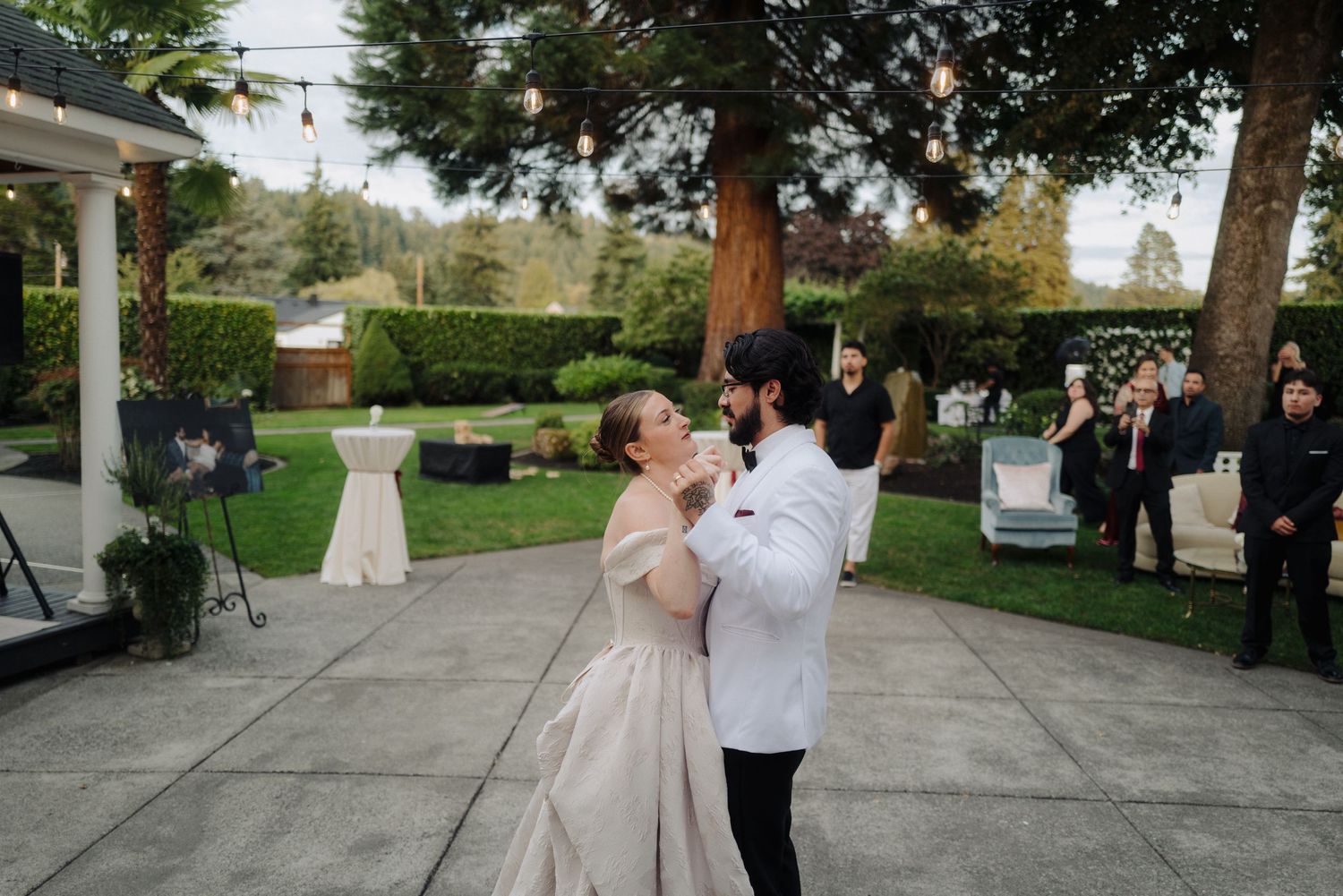 Outdoor wedding dance on a stone patio surrounded by lush gardens.
