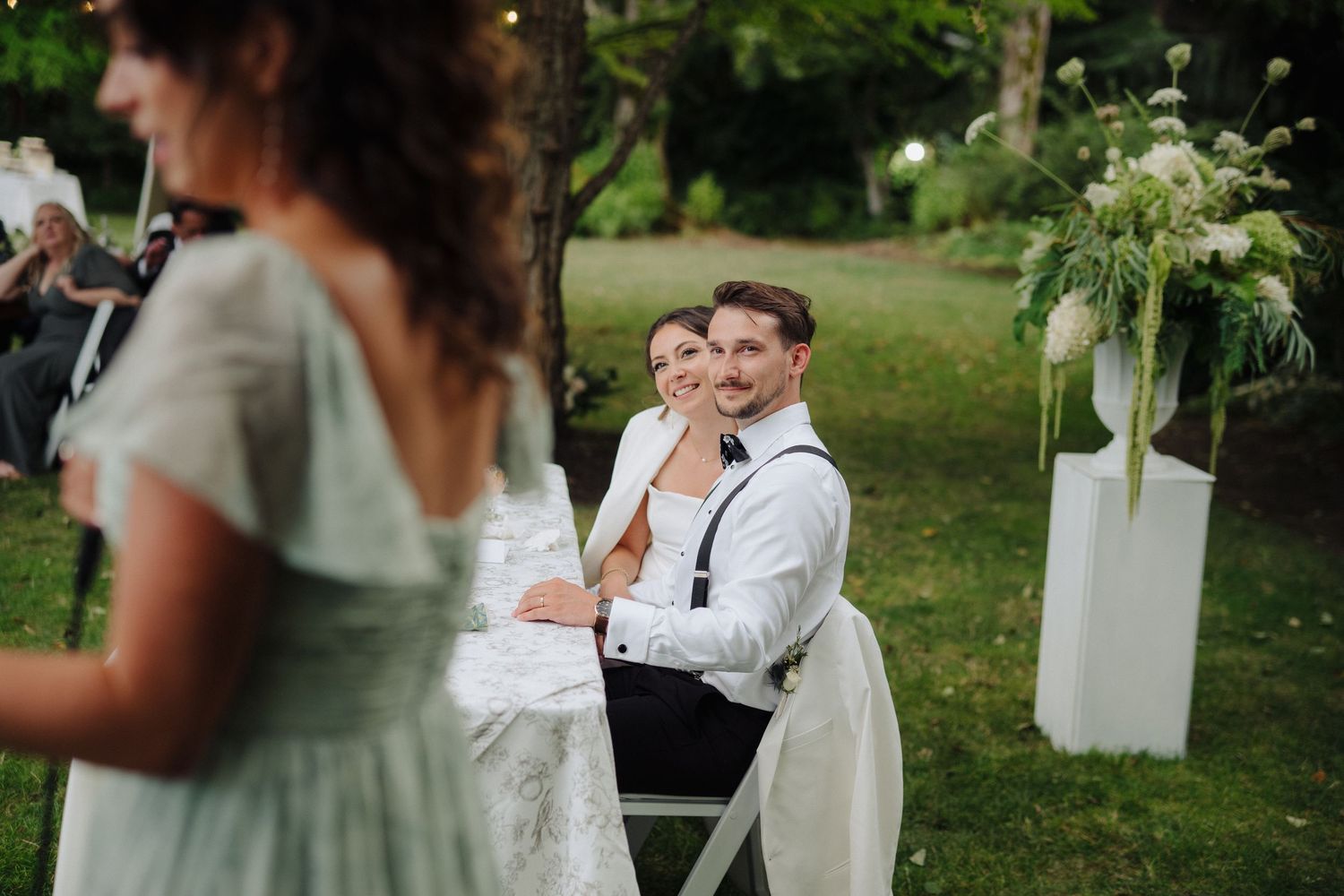 Wedding reception candid moment with guests and decorative floral arrangements.