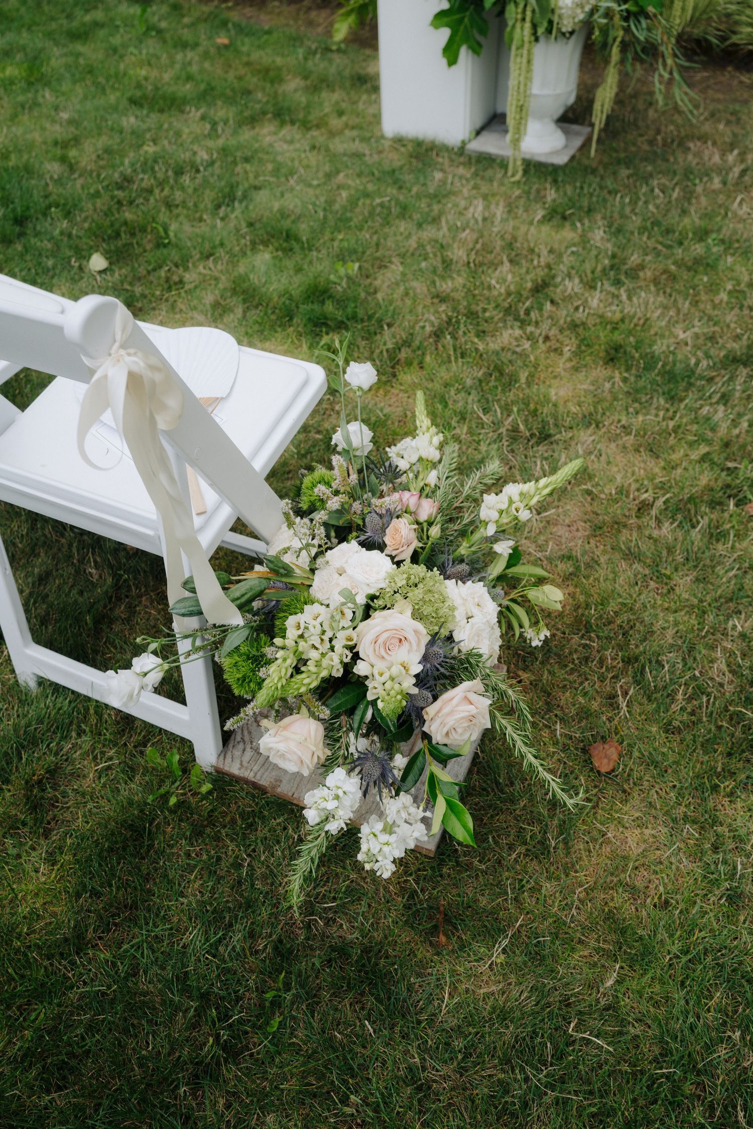 An elegant floral arrangement with white and pink roses decorates a white folding chair on grass.