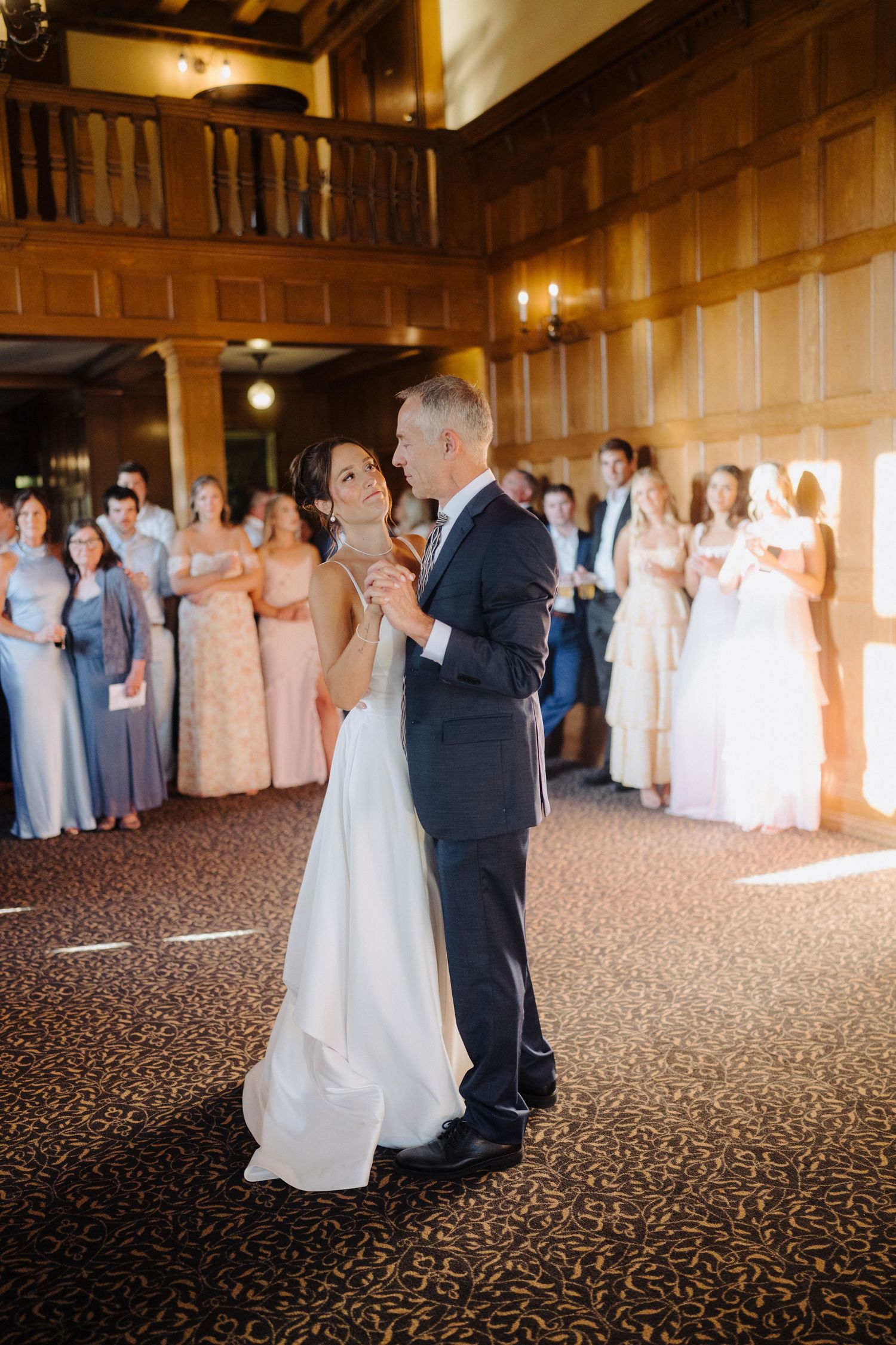Couples slow dancing in an elegant wood-paneled ballroom with warm lighting.