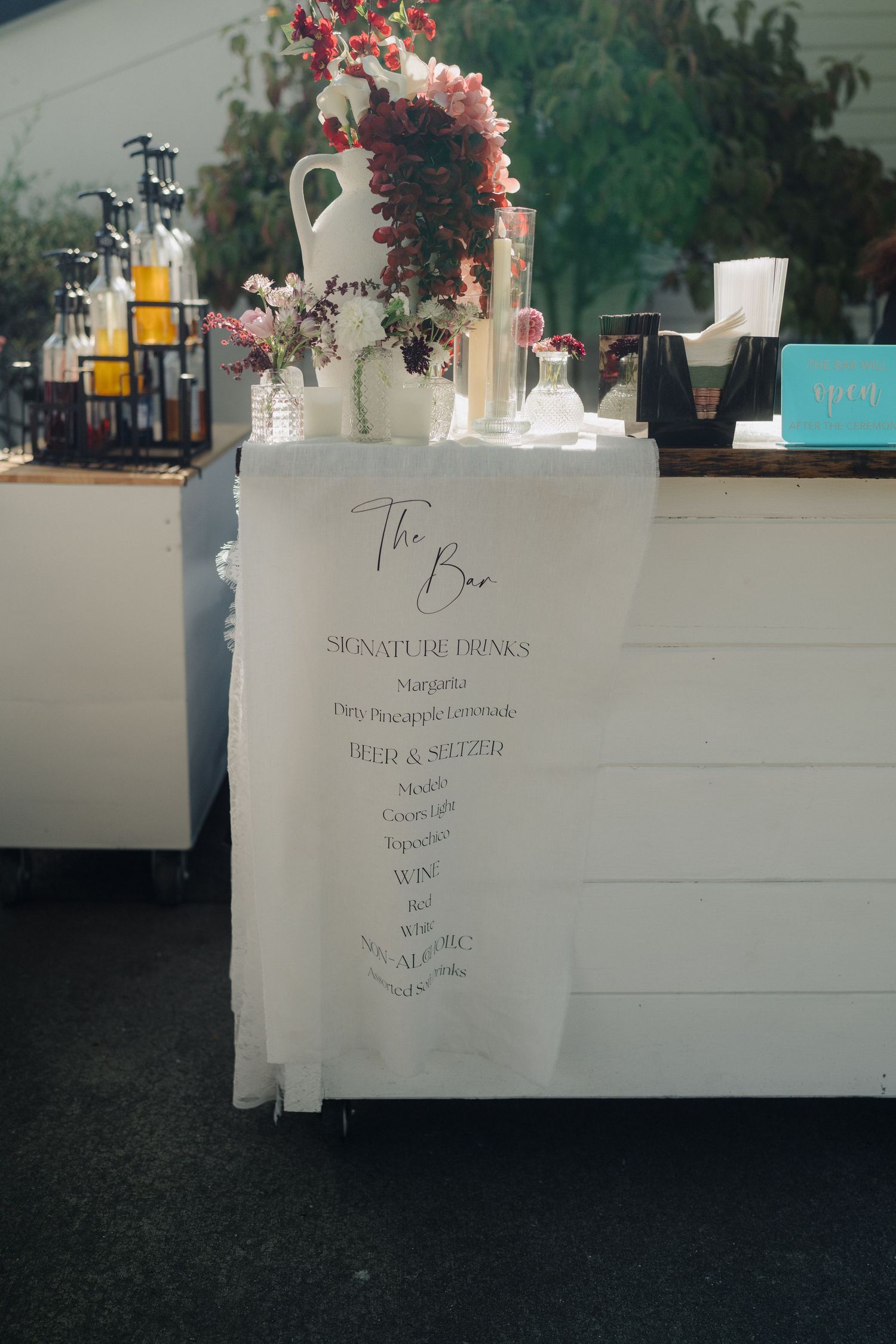 White wedding reception bar setup with floral decorations and drink menus.