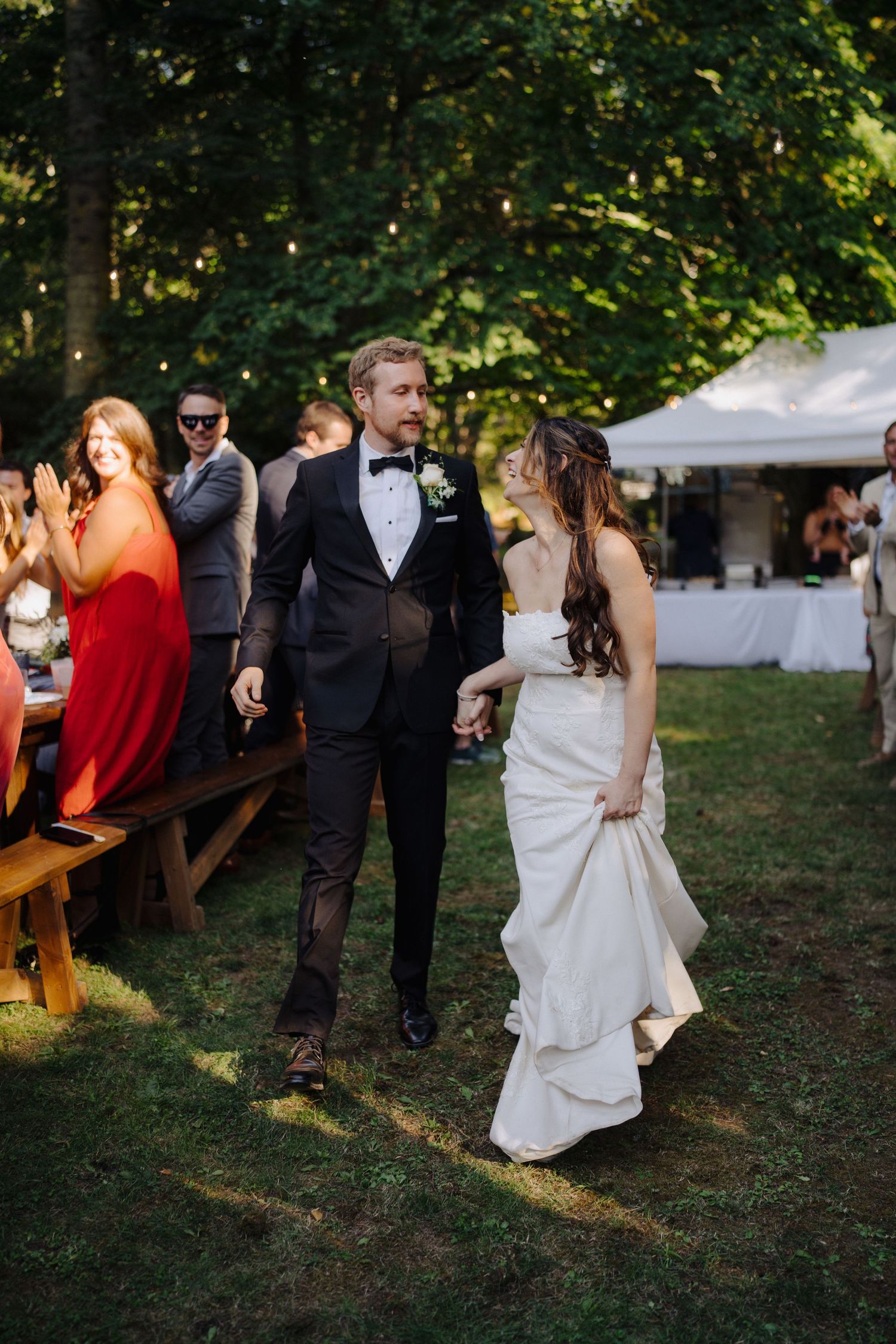 Wedding guests mingle on a grassy lawn with string lights and trees creating a romantic outdoor atmosphere.