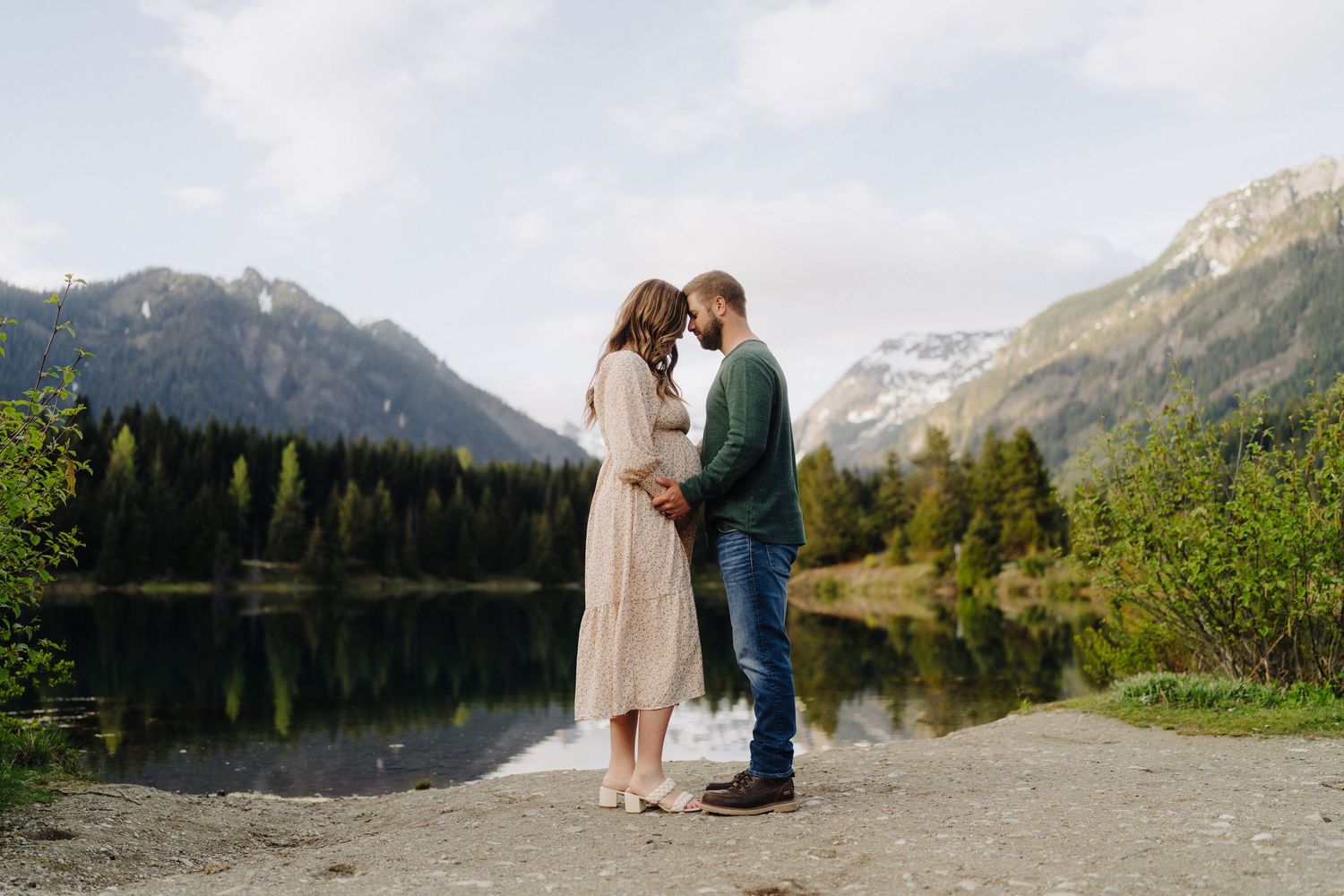 A couple shares an intimate moment by a mountain lake with snow-capped peaks in the distance.
