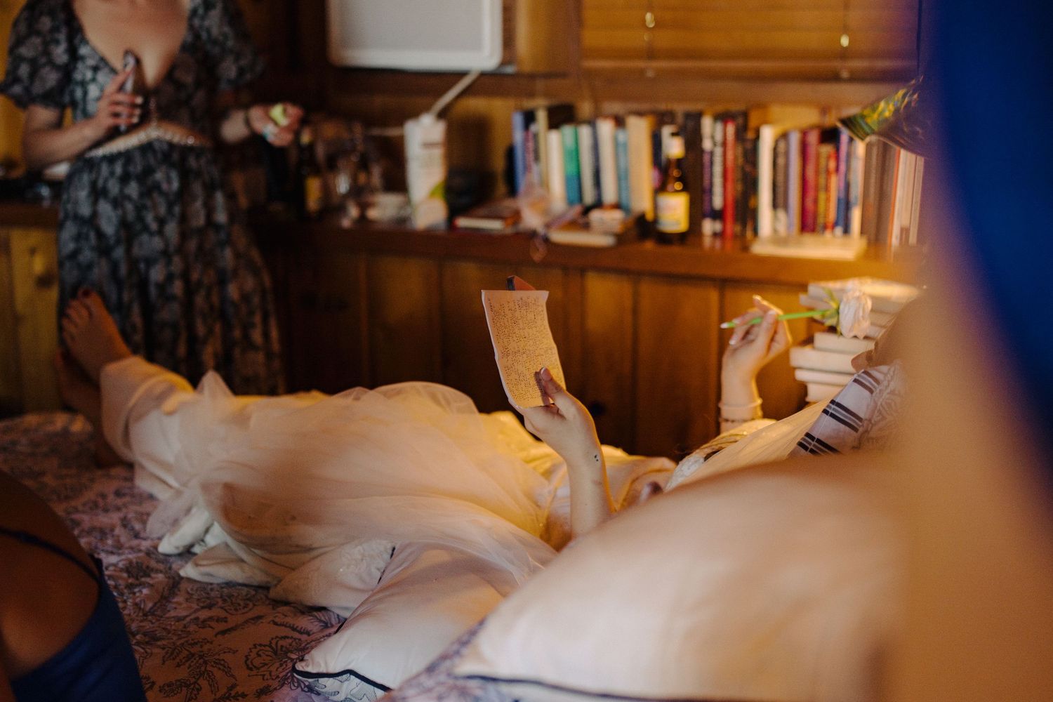 Person reading book while relaxing on couch with bookshelf in background.