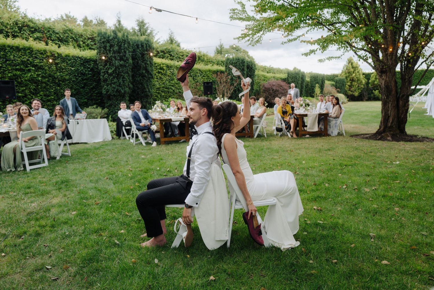 Outdoor wedding reception setup with tables and chairs on a grassy lawn under trees.