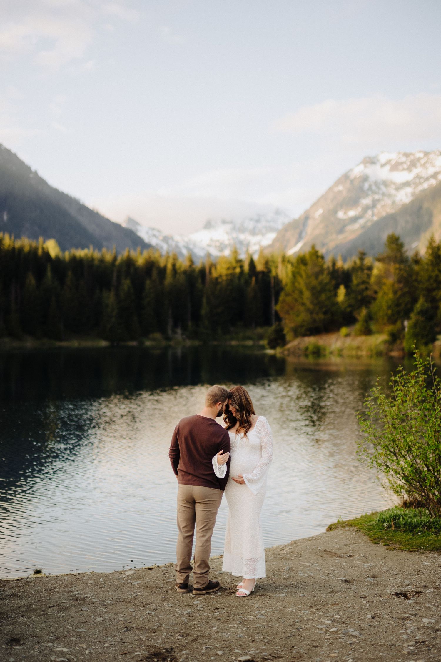 A romantic proposal scene unfolds on a rocky beach with mountains and a serene lake in the background.
