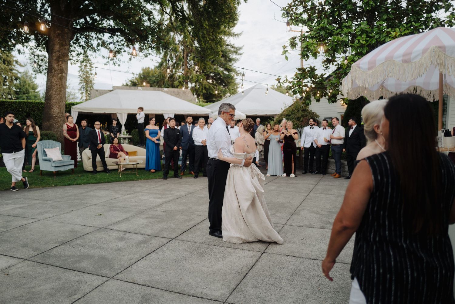 A couple dances together at an outdoor wedding reception while guests watch from the sidelines.