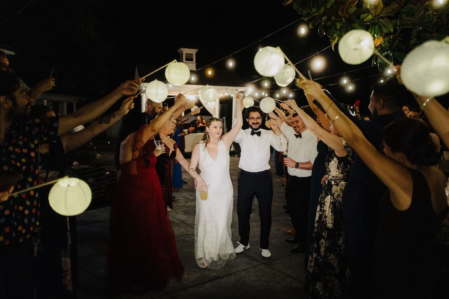 Wedding guests dancing under glowing paper lanterns at nighttime outdoor reception.