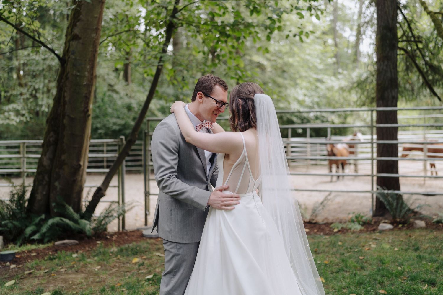 A romantic wedding couple embraces and kisses in a serene forest setting with a white veil flowing in the breeze.