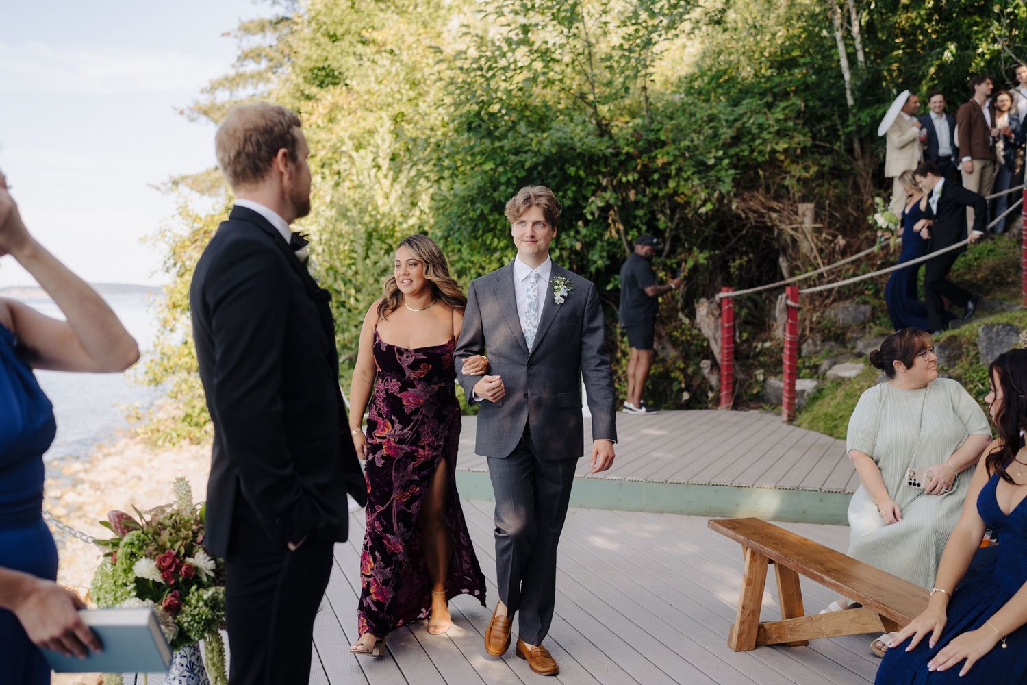 Wedding guests gathered on a wooden deck overlooking the water during an outdoor ceremony.