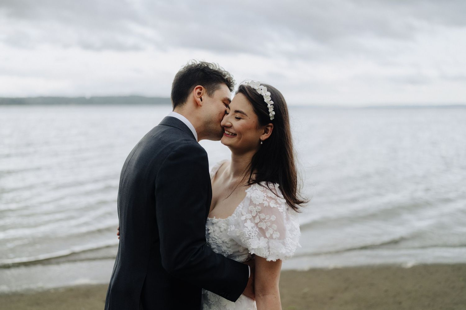Intimate moment between newlyweds against moody coastal backdrop with waves.