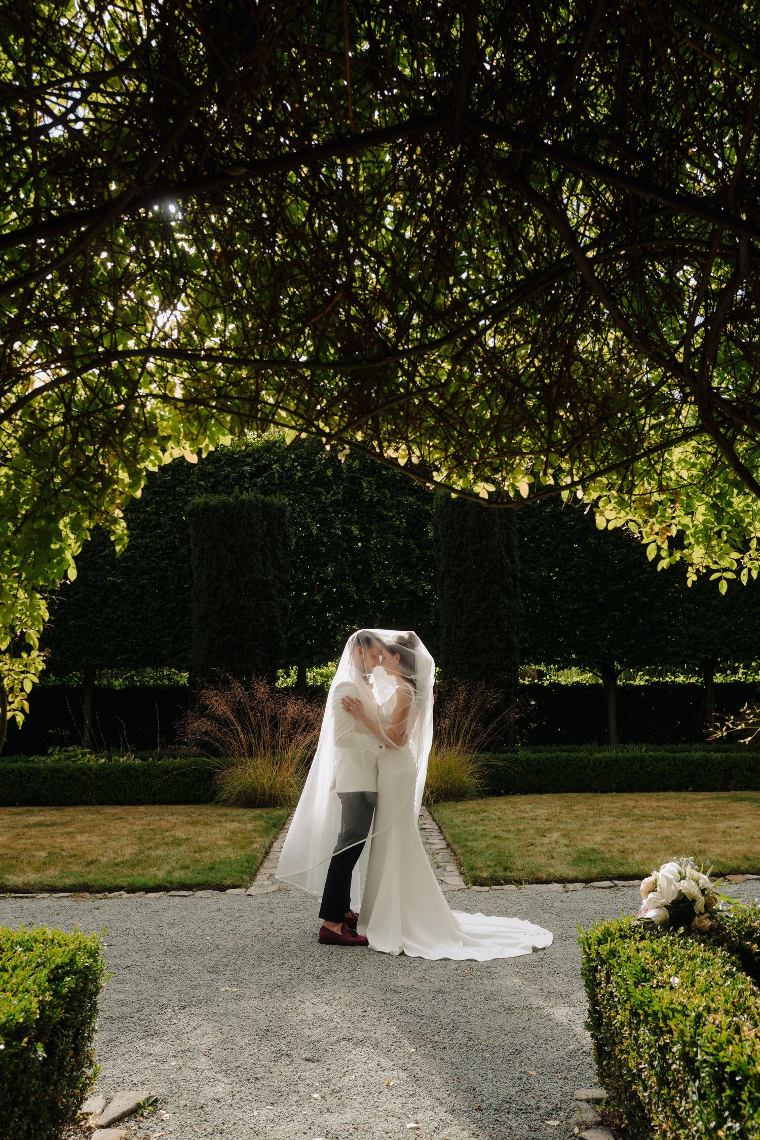 Garden wedding ceremony setup with sunlight filtering through tree canopy overhead.