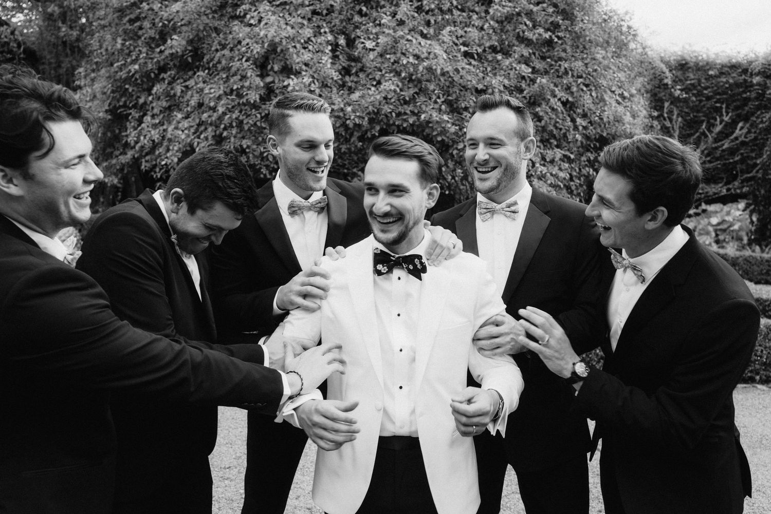 Black and white photo of wedding party sharing laughs during formal portraits outdoors.