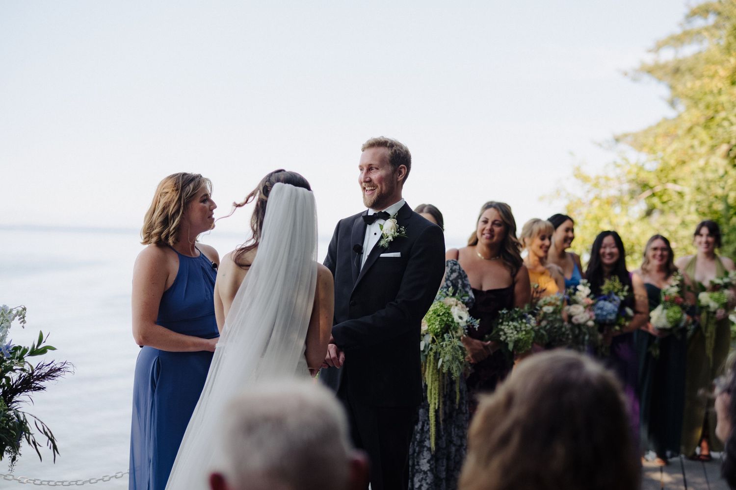 Wedding celebration on a sunny deck with trees and water in the background.