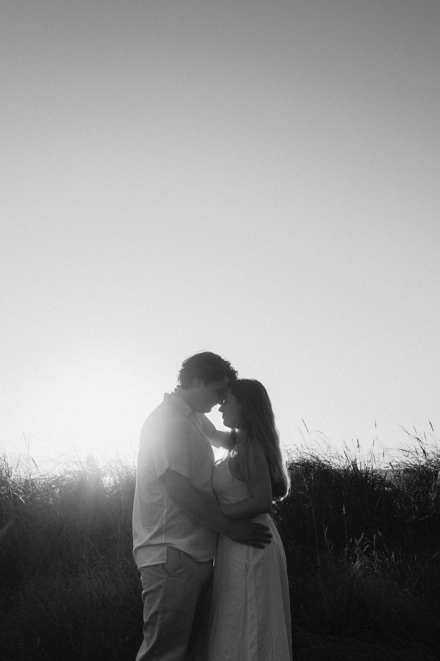 Silhouetted couple sharing intimate moment against bright sky.