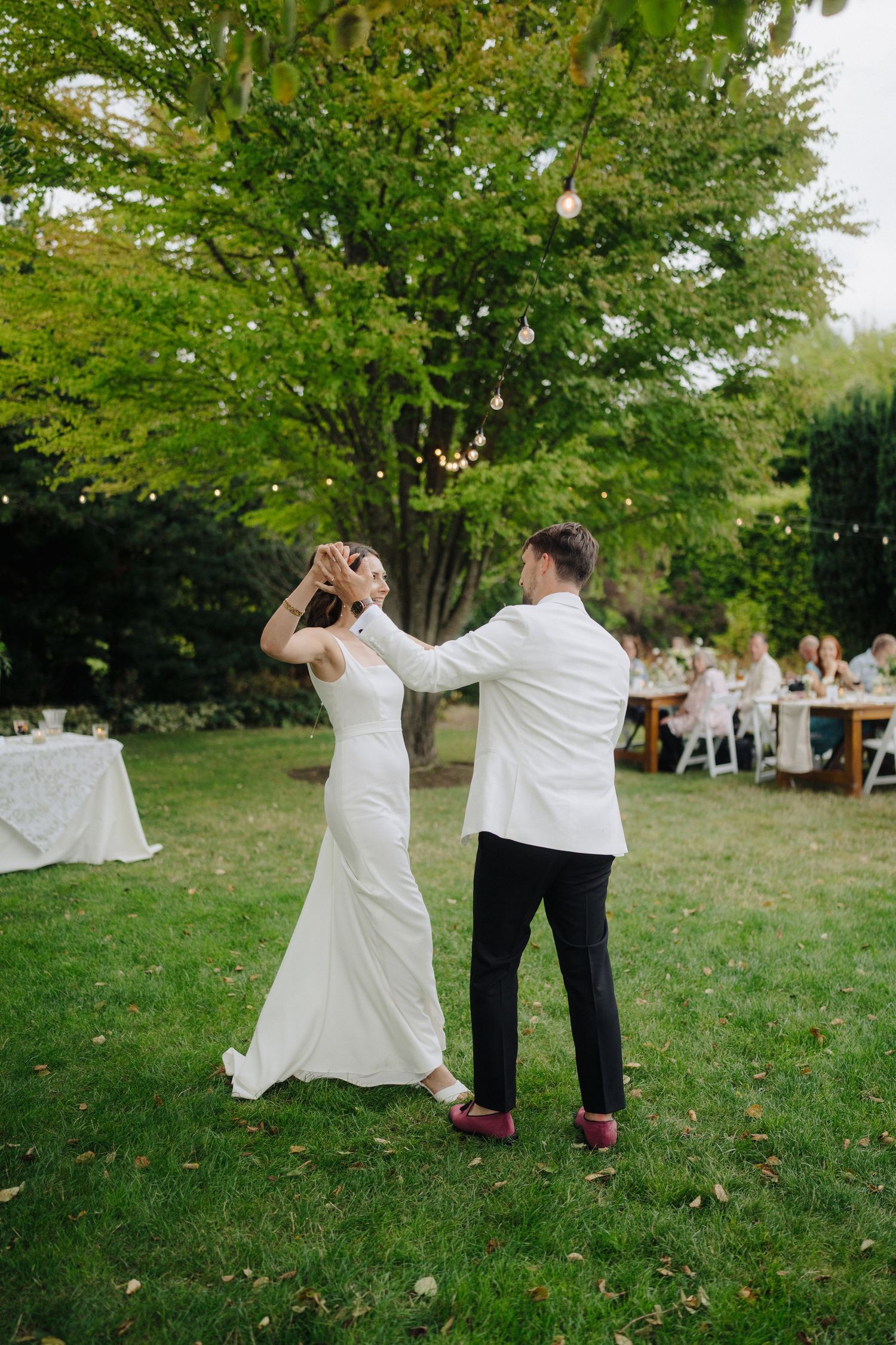 Wedding couple dances playfully on the grass during their outdoor reception celebration.