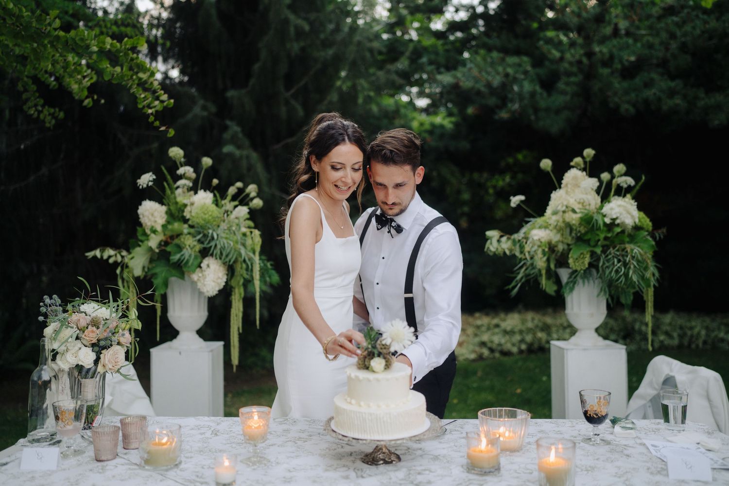 Elegant wedding table setting with white floral arrangements and candles in garden.
