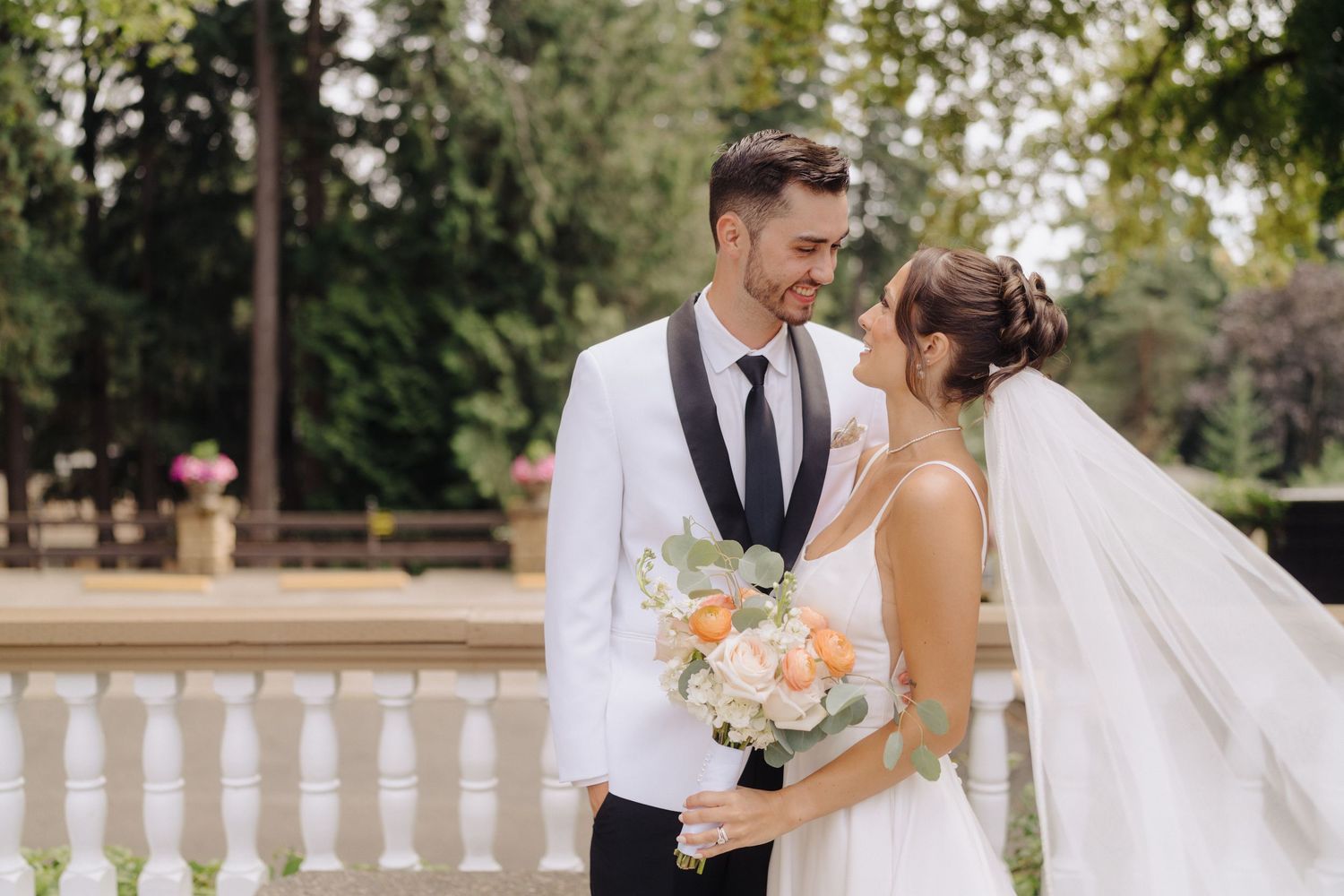 Wedding couple embracing in a lush garden setting with white balustrade railing.