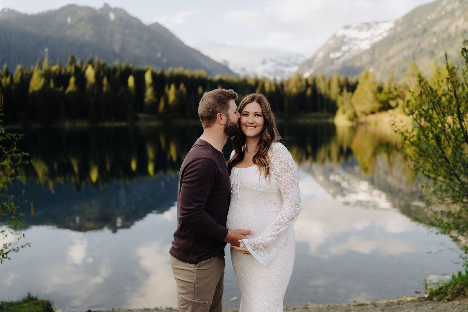 A romantic lakeside photo session with mountains and evergreen forest creating a stunning backdrop.