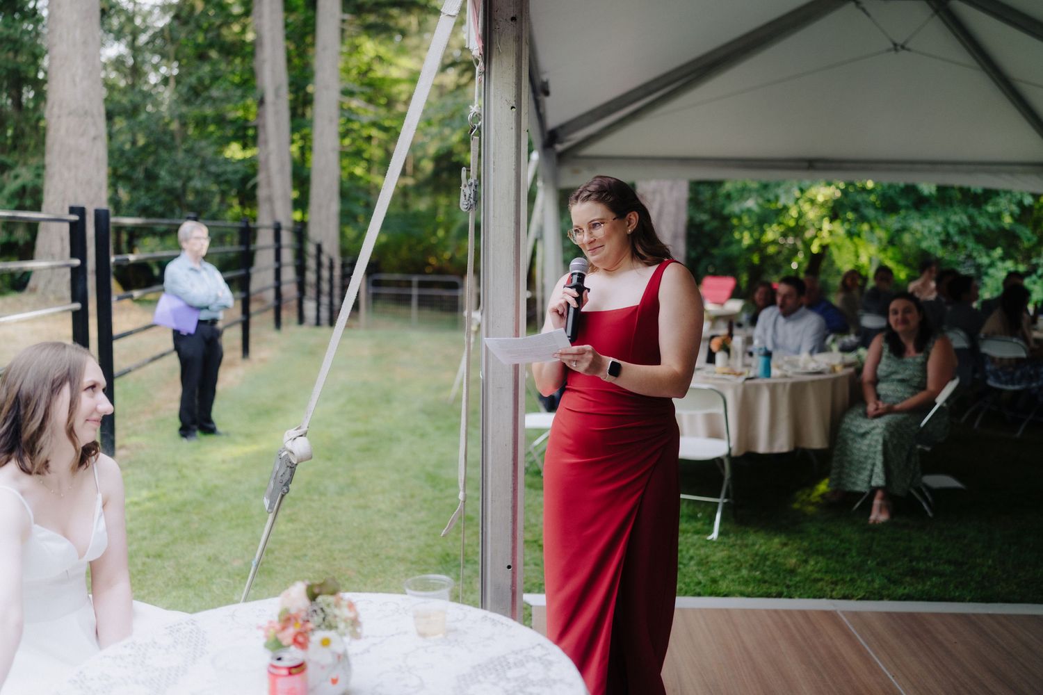 Wedding reception scene with guests gathered under a white tent on a sunny day.