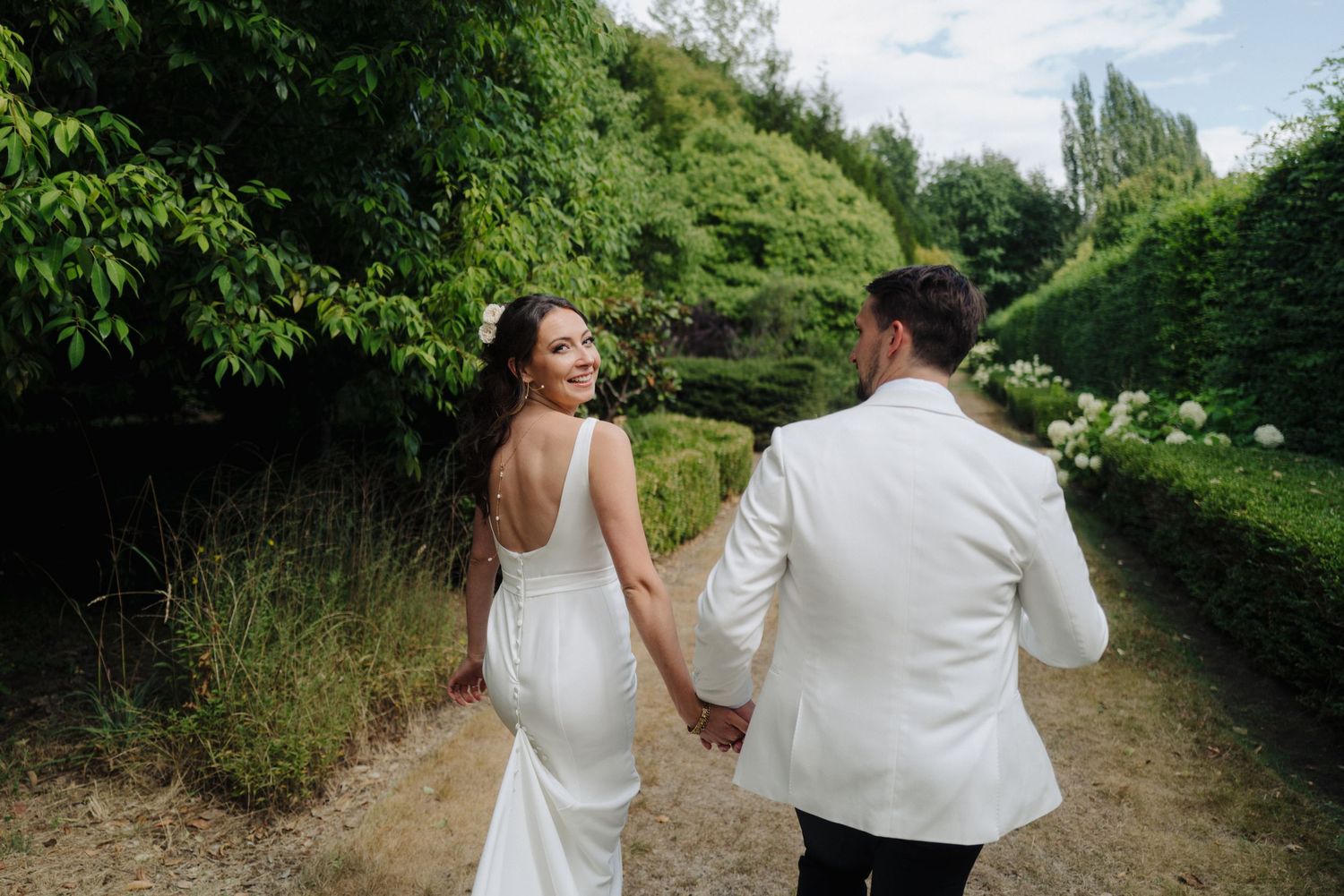Couple walks hand in hand down a lush green garden path during their wedding.