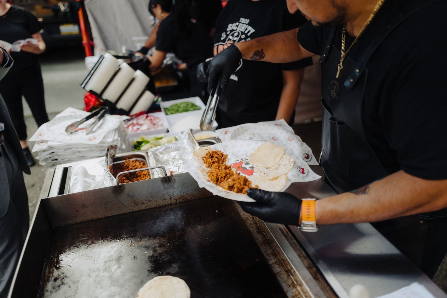 Wedding catering staff preparing food at buffet station under white tent.
