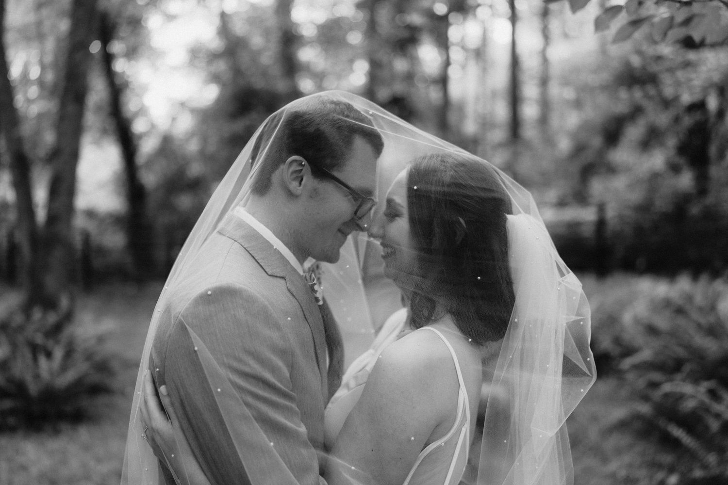 Black and white romantic portrait of a couple in a wooded outdoor setting.