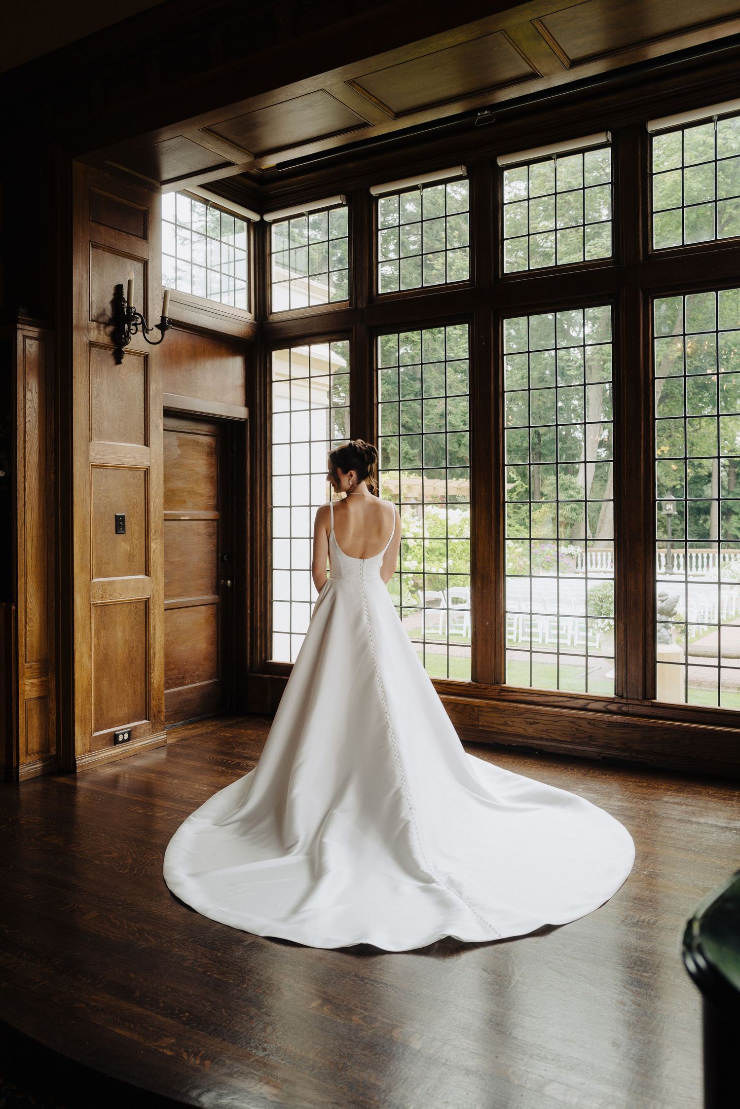 Dramatic bridal portraits showing the sweep of a white wedding gown in a wood-paneled room with large windows.