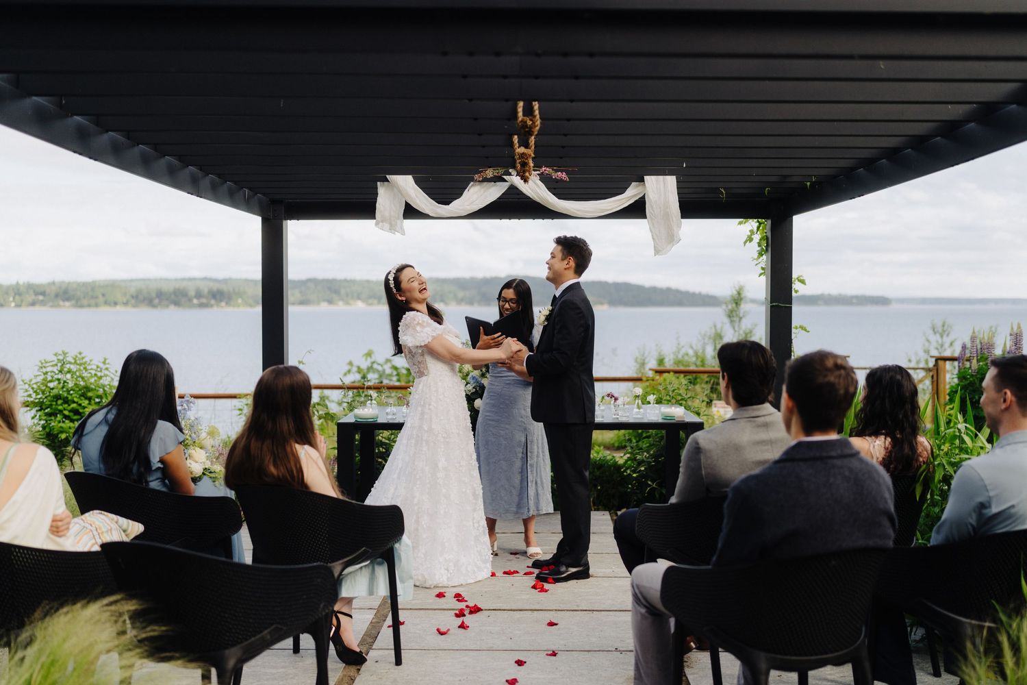Wedding guests seated under a dark covered pavilion during an outdoor ceremony.