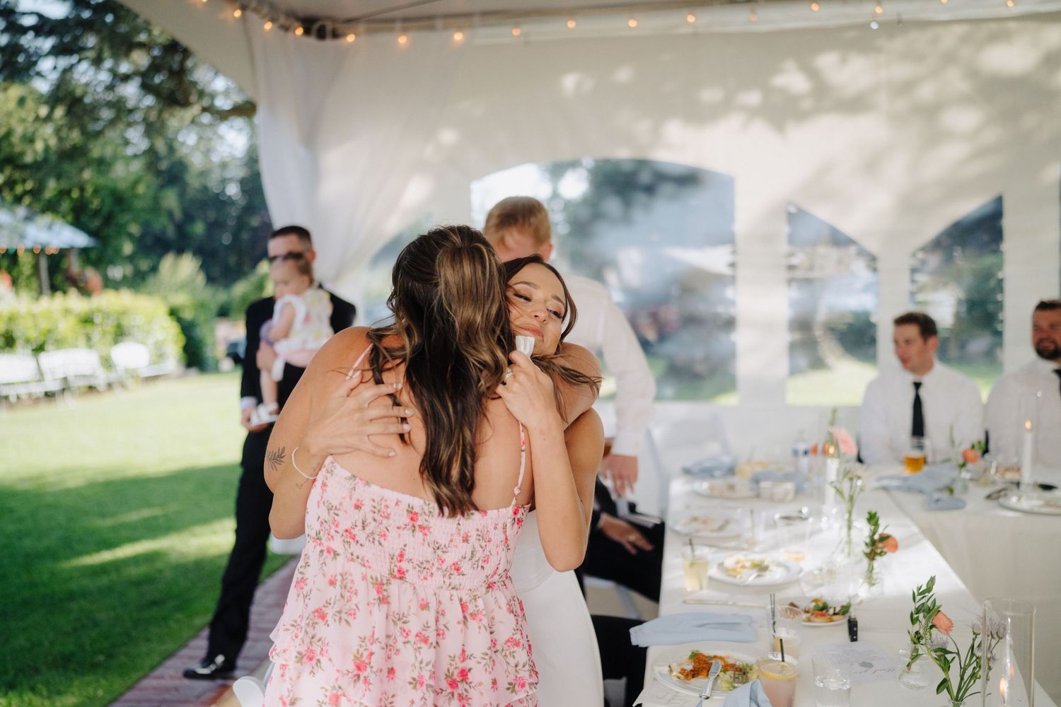 Wedding reception under a white tent with floral decorations and string lights.