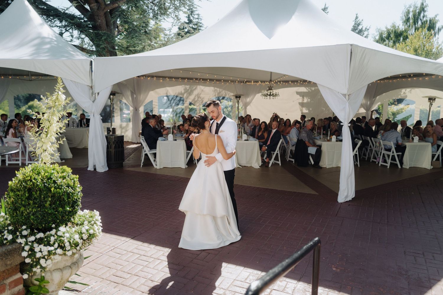 White wedding tent set up on brick patio with floral decorations and draping.